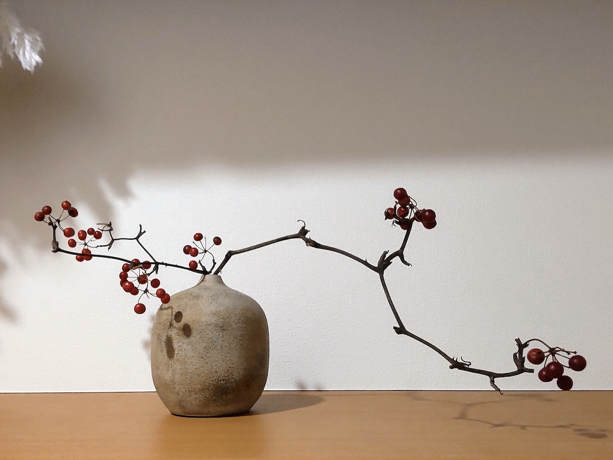 A dried vine plant with red berries arranged in a shriveled potato-shaped vase