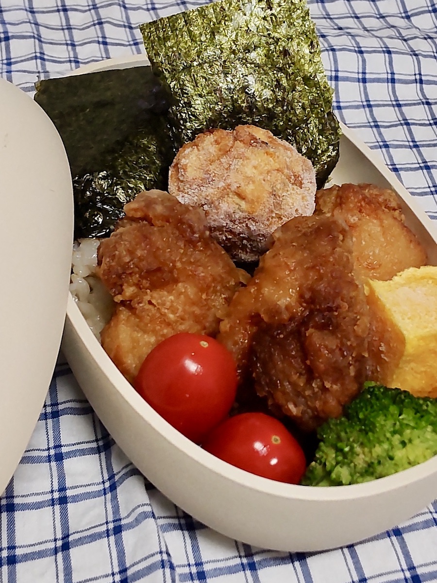 Bento box with fried chicken, tamagoyaki(Japanese Omelet), tomato, broccoli, and rice topped with seaweed