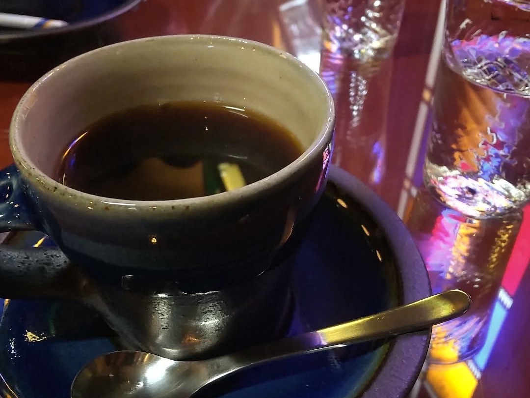 Coffee in a handmade ceramic and glass cup, with stained-glass colors reflecting on the surface, creating a cozy and artistic vibe