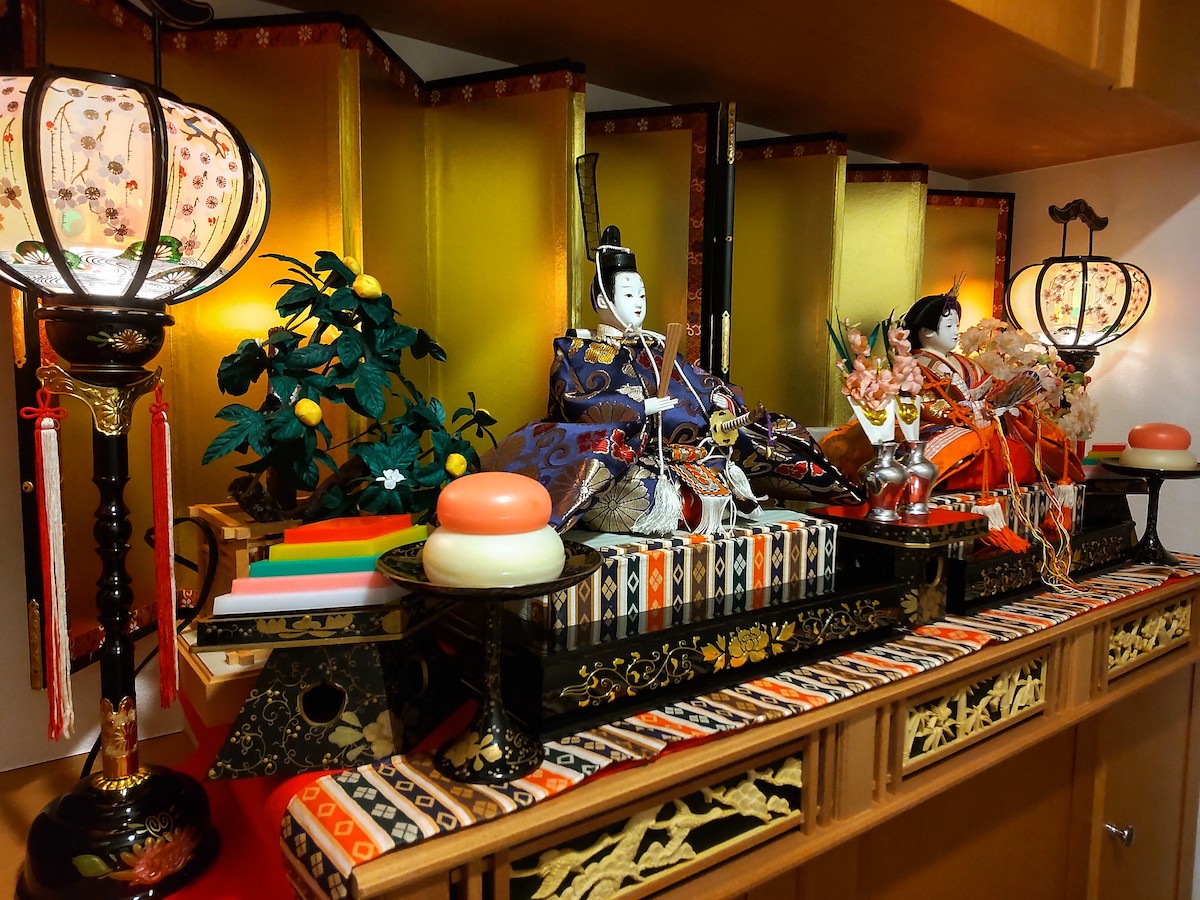 Hina doll display in the entryway with gold folding screen, lanterns, flowers, and a pair of dolls