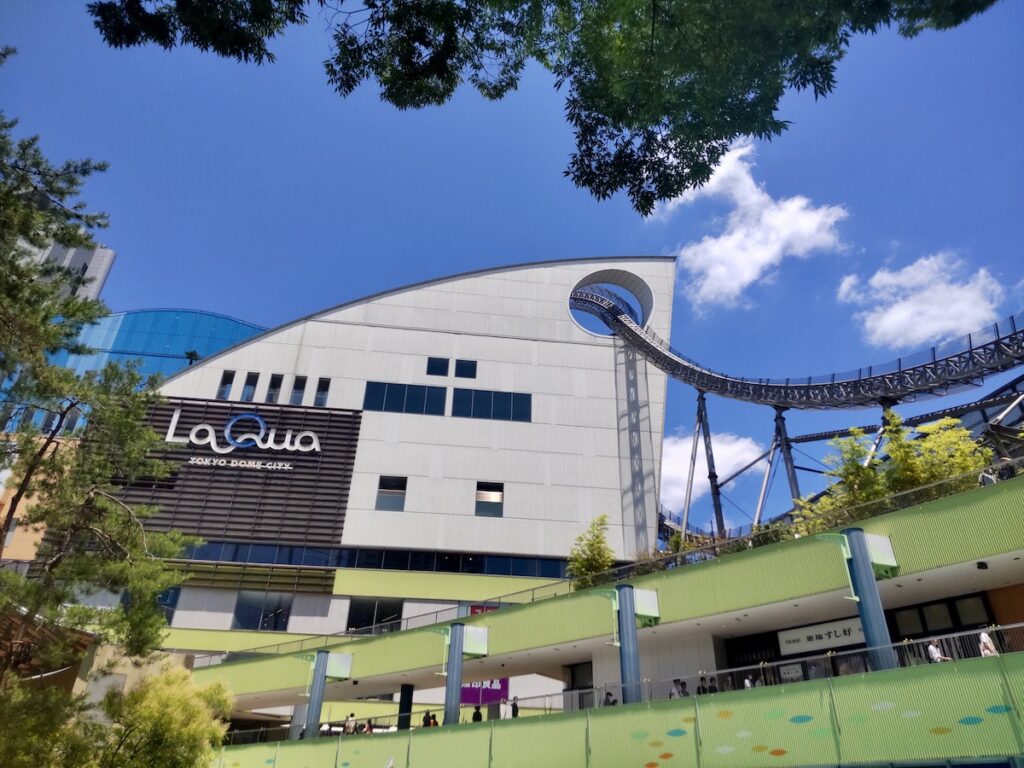A roller coaster track passing through a large circular hole in a building at Tokyo Dome City