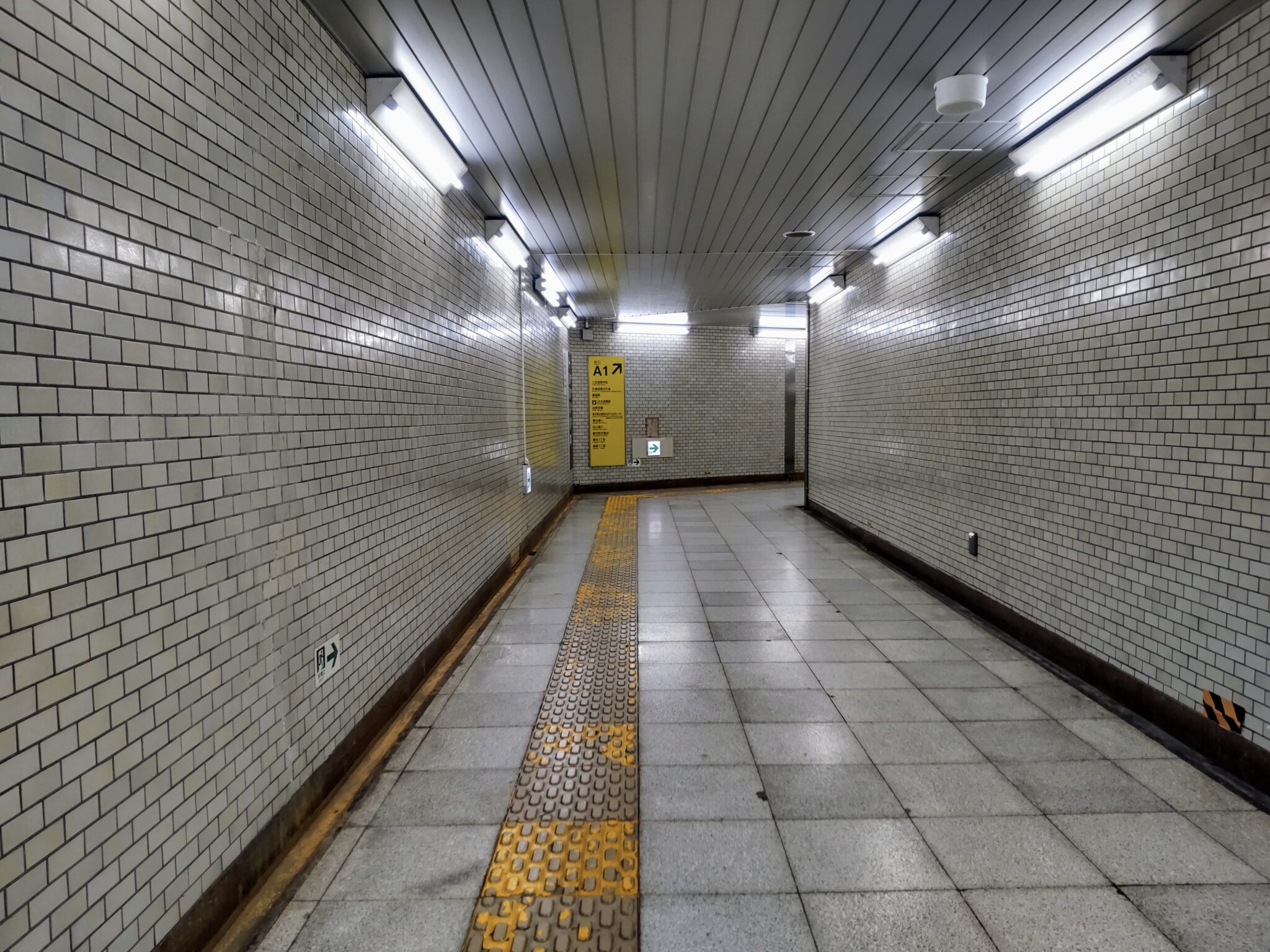 Dim Japanese subway path with white tiles and yellow signs