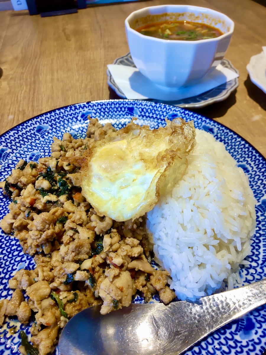 Gapao rice topped with a fried egg, with Tom Yum Goong in the back