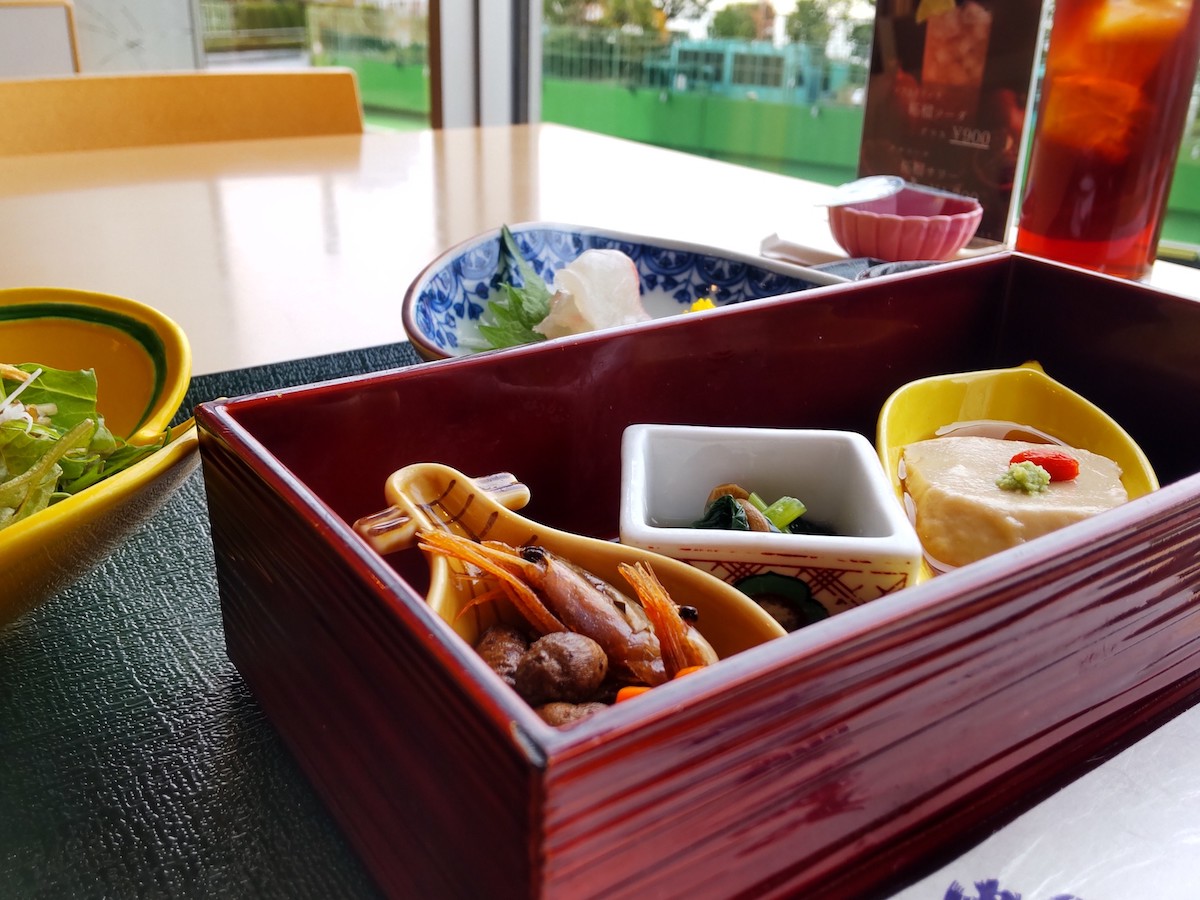 Three Japanese small bowls in a square wooden frame, with salad and sashimi on the side