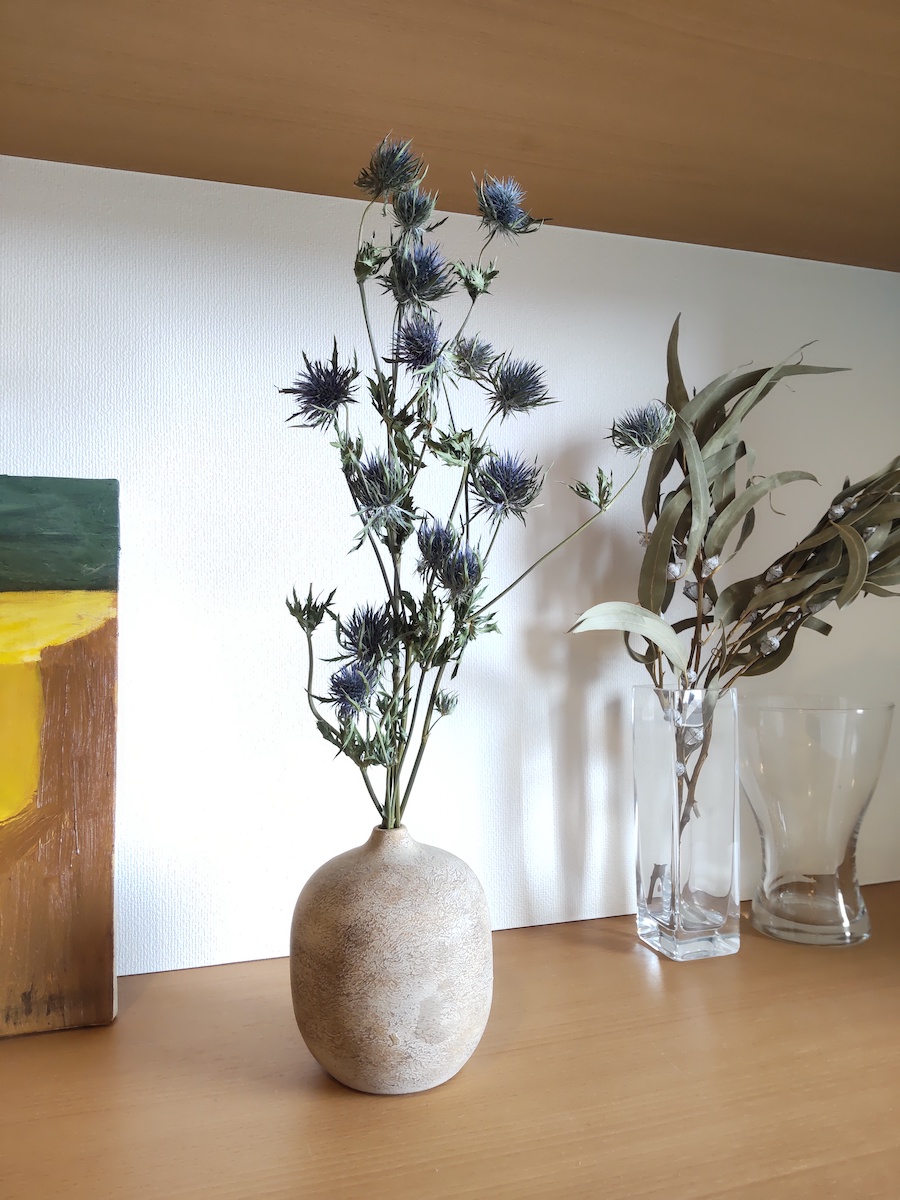 Summer entryway display with blue dried flowers in a rustic brown vase, and eucalyptus dried flowers in a clear glass vase