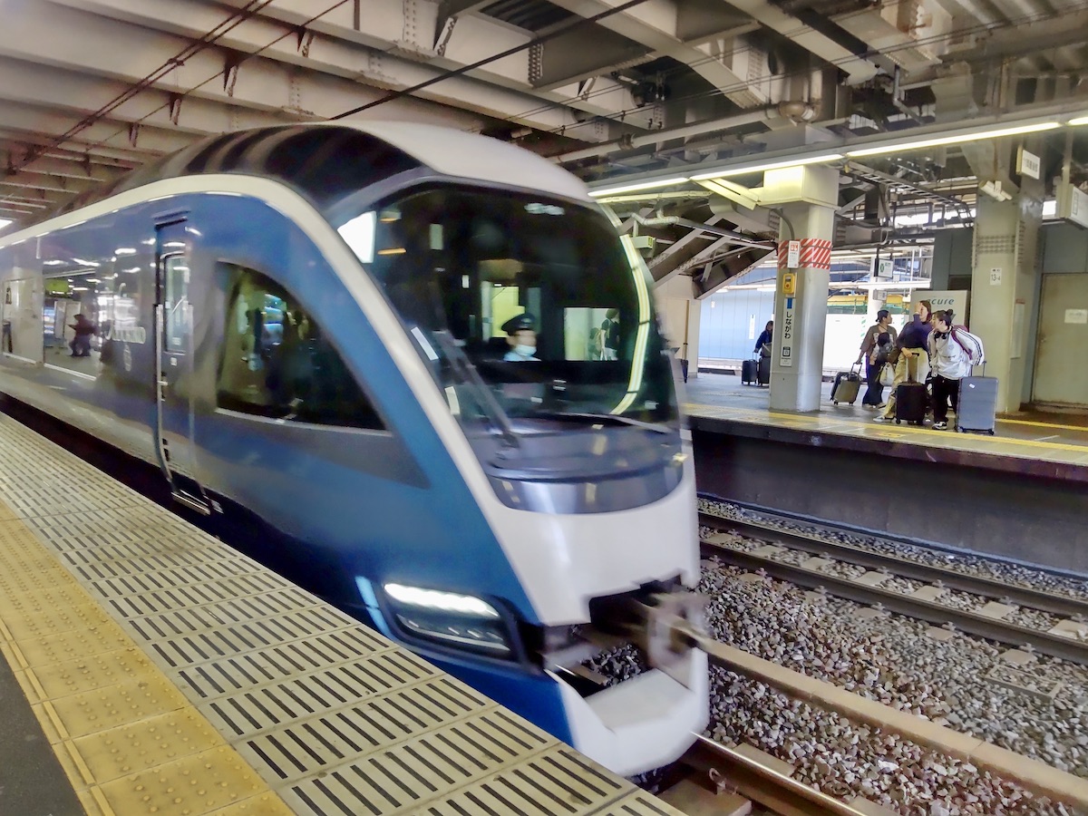 A sleek dark blue-green streamlined train arriving at a station railway platform