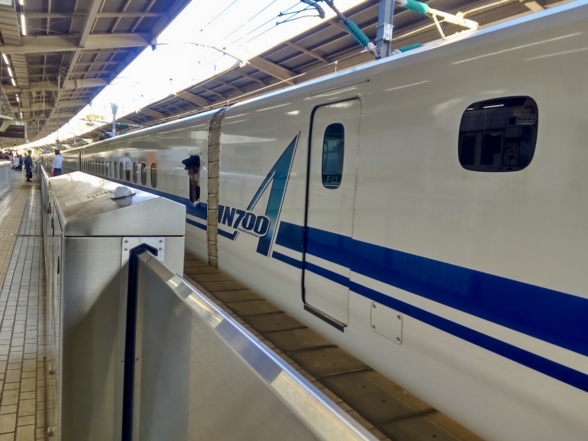A shiny white and blue Shinkansen train stopped at a railway platform