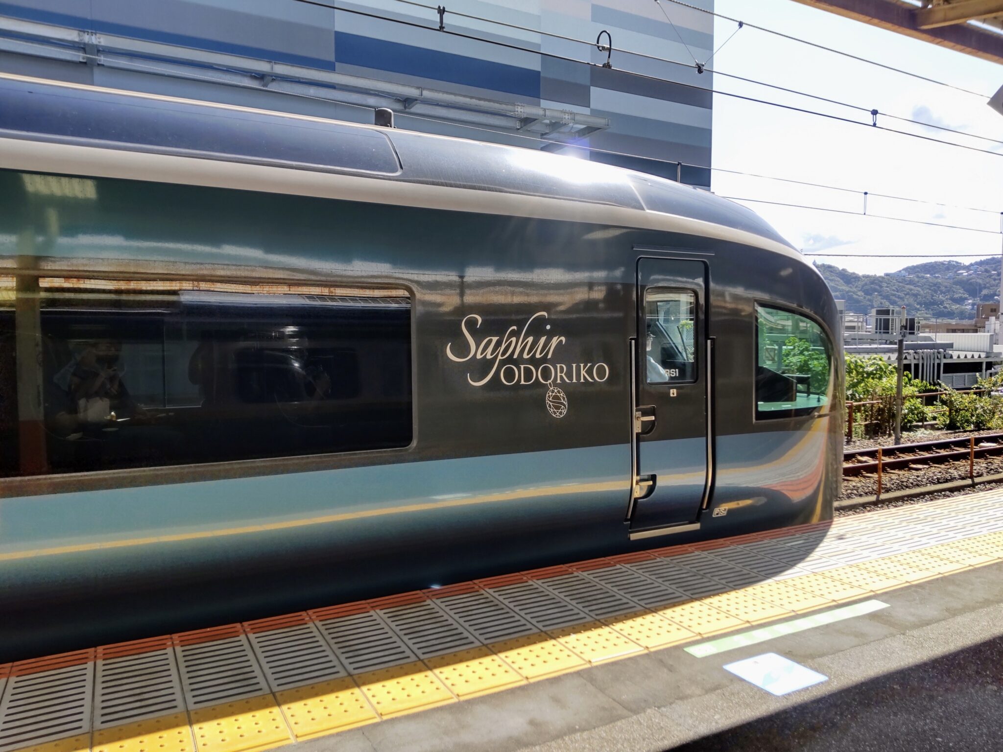 A deep green rounded train at a platform illuminated by the morning sun