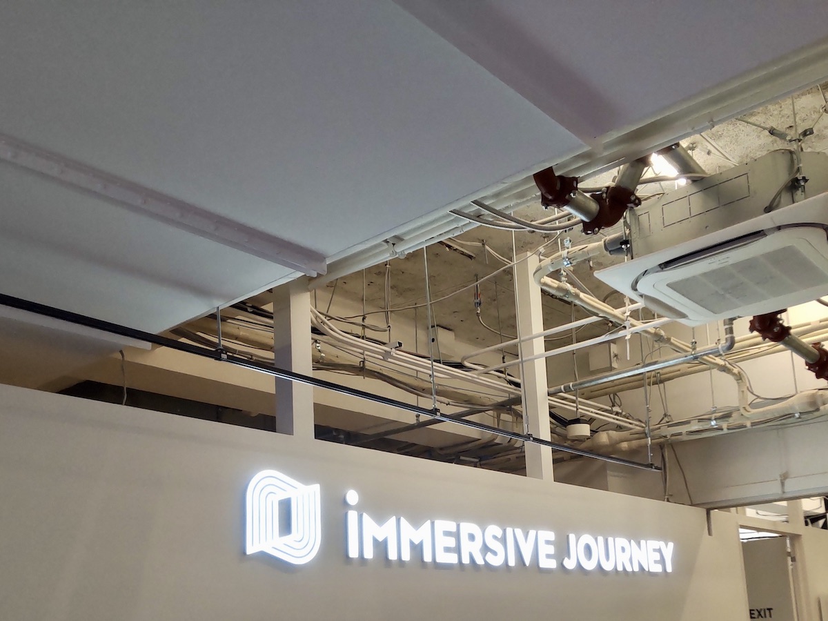 A neon sign above the reception desk reading 'Immersive Journey'
