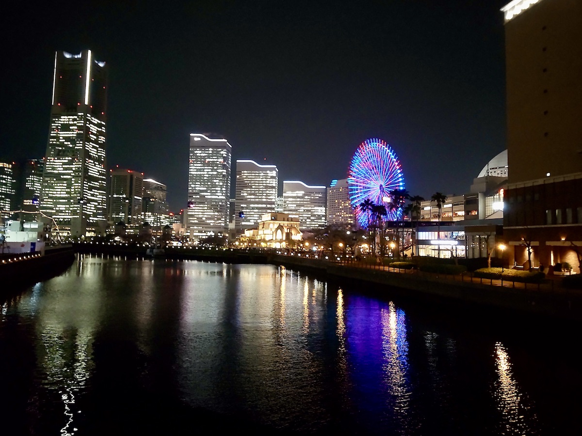 Night view of skyscrapers and a Ferris wheel reflecting on the river surface