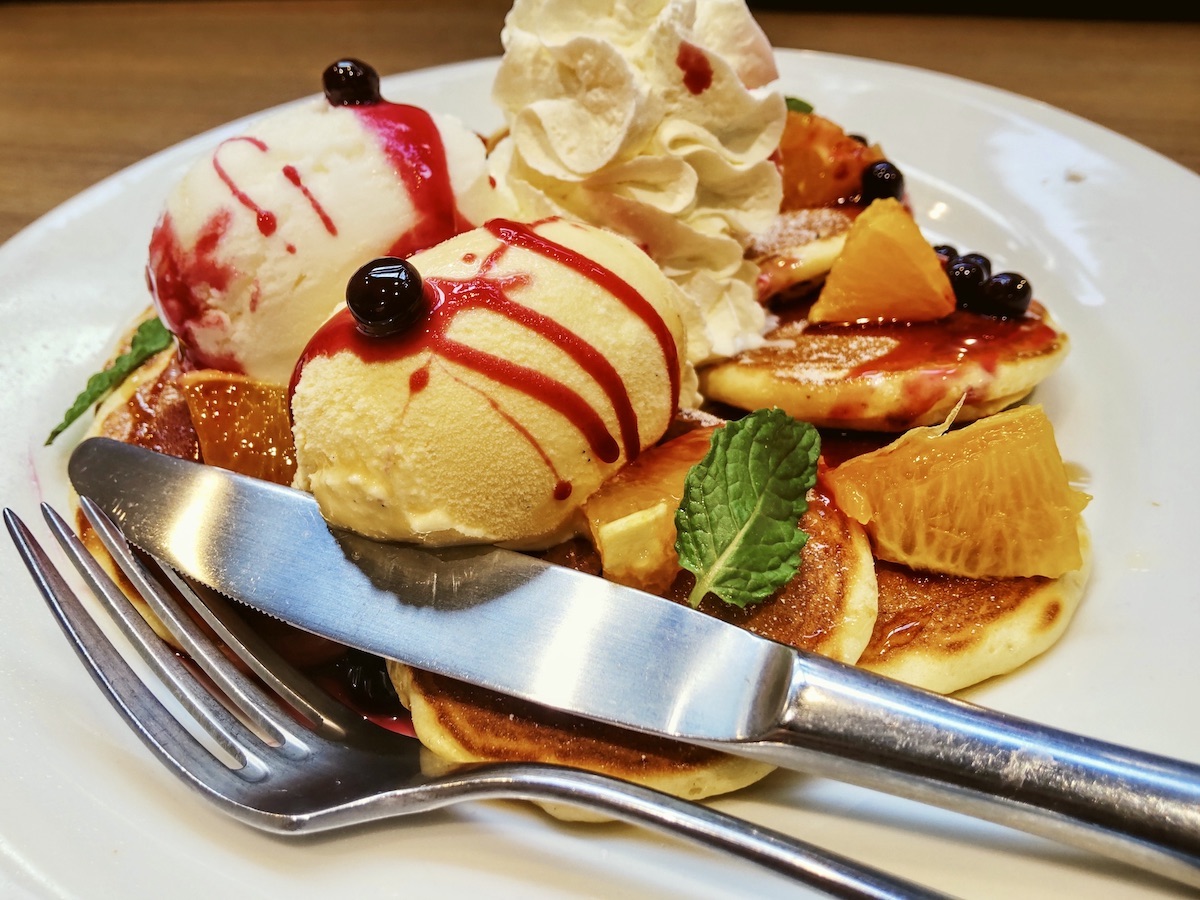 Eight small pancakes spread on a plate with two scoops of ice cream and fruit