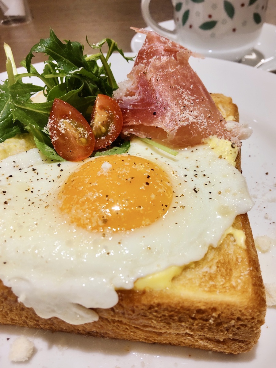 Toast topped with a soft-boiled egg, prosciutto, vegetables, and grated cheese