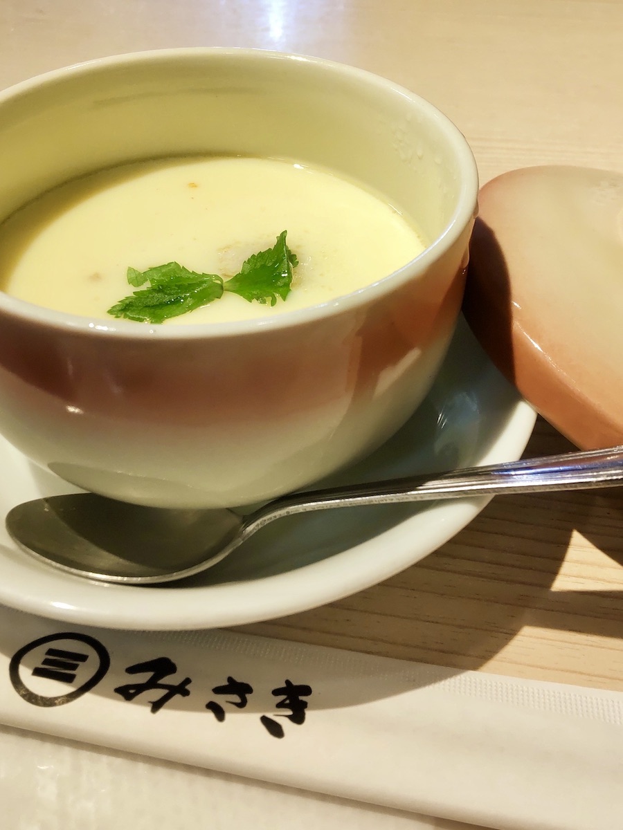A savory steamed egg custard in a pink bowl topped with mitsuba