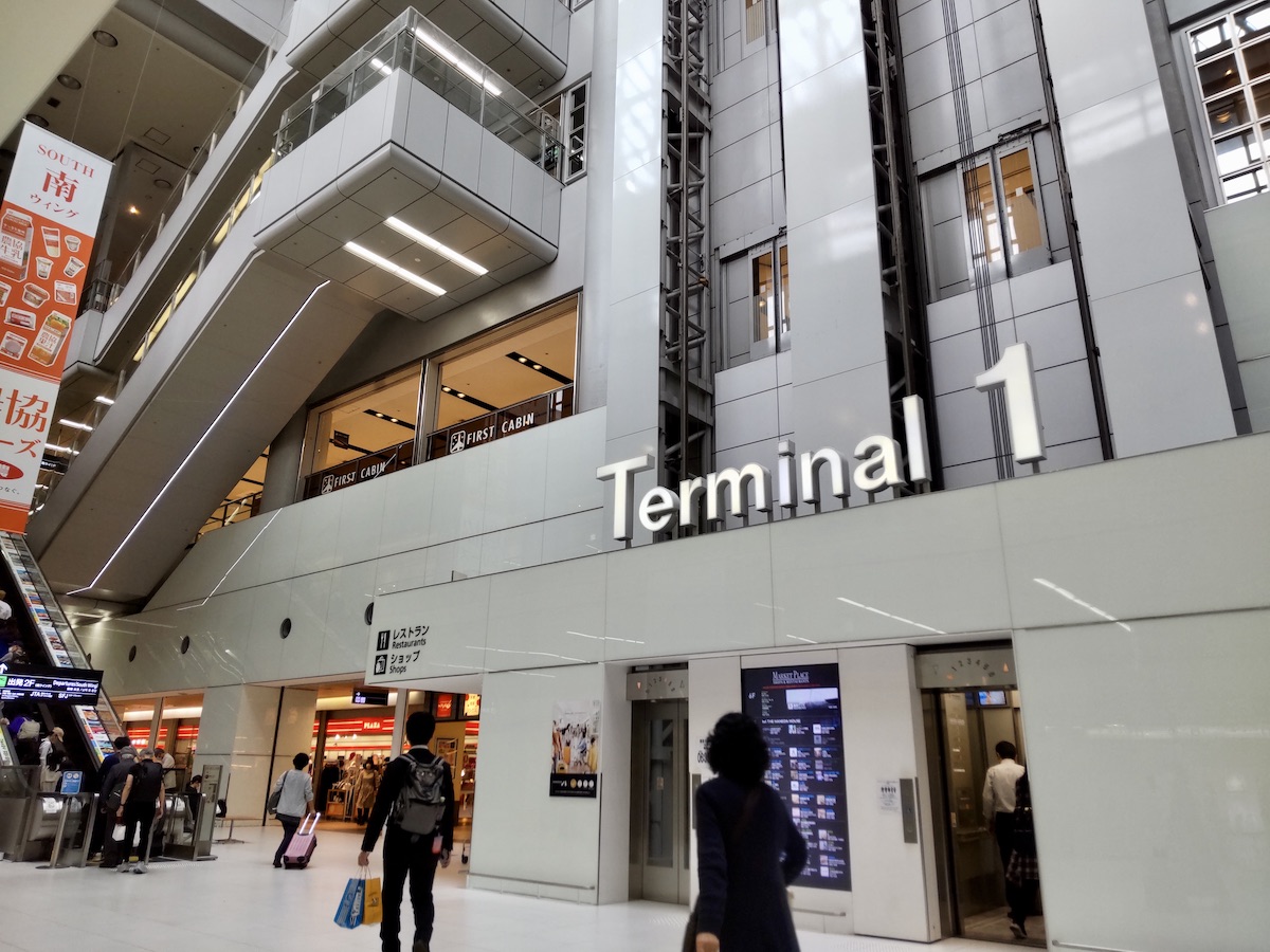 A large Terminal 1 sign mounted directly above the elevator, with nearby escalators