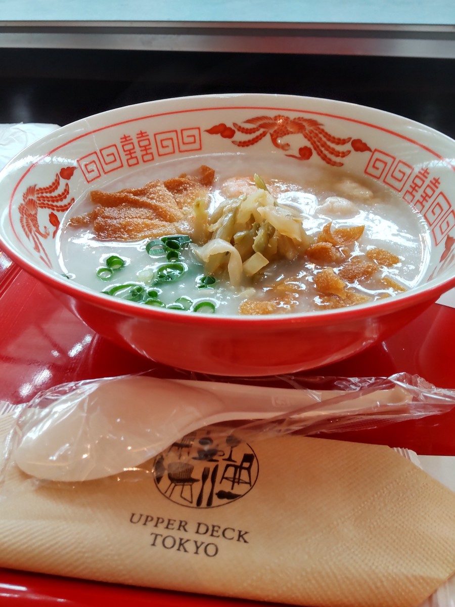 A red bowl of congee topped with zha cai and green onions on a tray