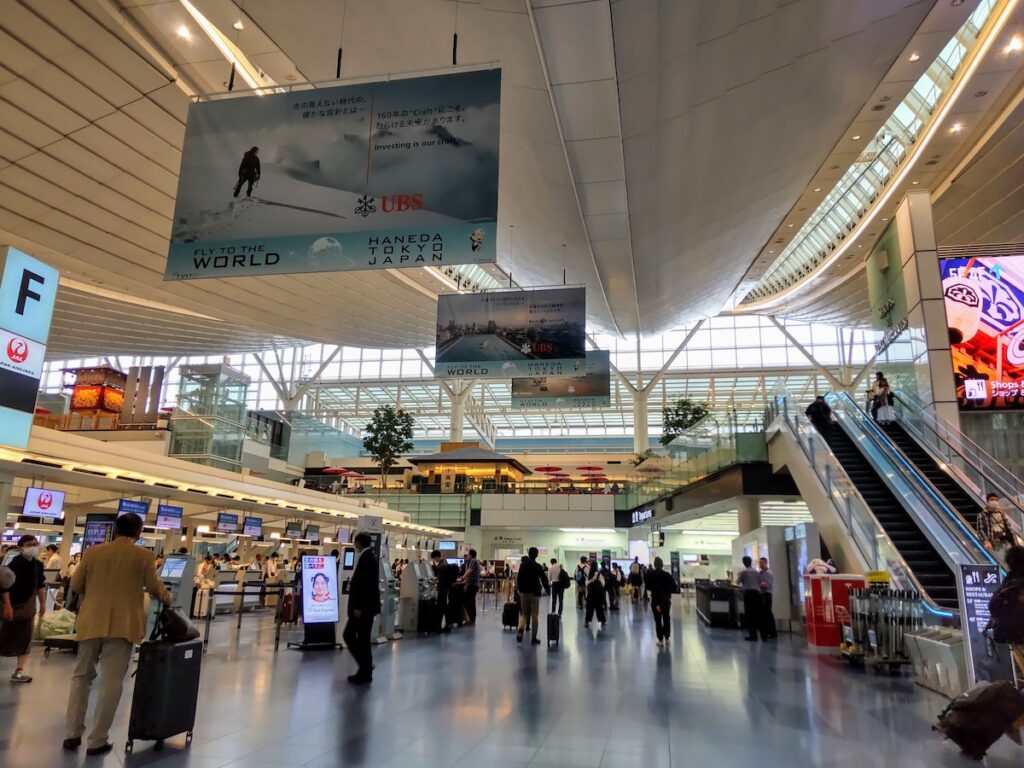 A spacious airport terminal with check-in counters, escalators, and people walking through