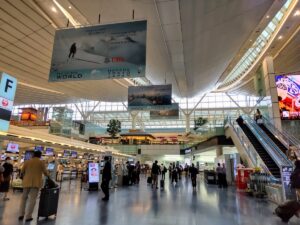 A spacious airport terminal with check-in counters, escalators, and people walking through