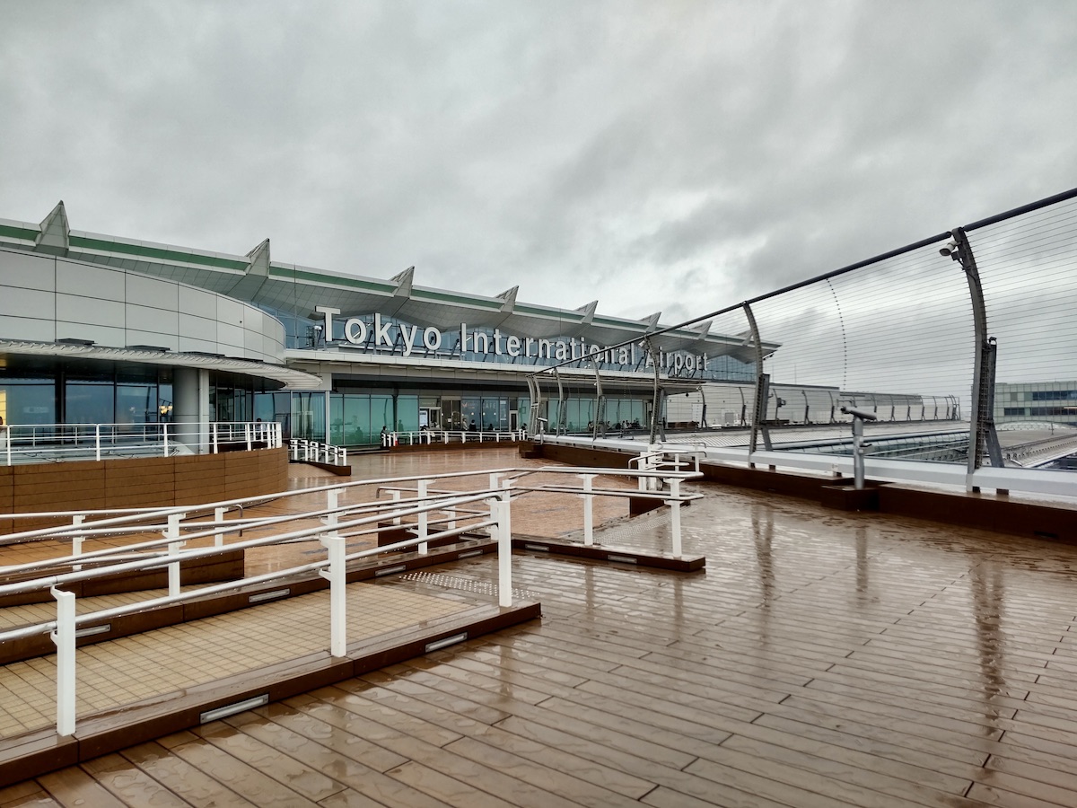 A rainy observation deck featuring a large Tokyo International Airport sign in the background