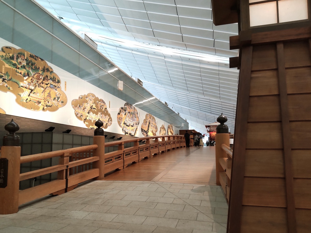 An indoor traditional Japanese wooden bridge set against a wall featuring a classic Japanese painting