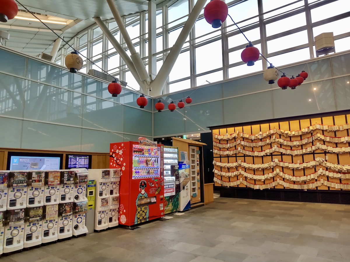 A wall hung with numerous wooden plaques behind a row of vending and capsule toy machines