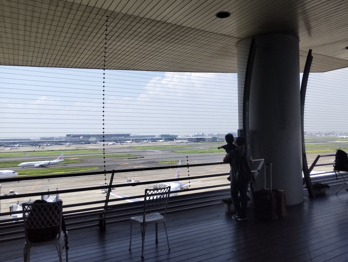 A covered observation deck looking through a fence at parked airplanes on the apron