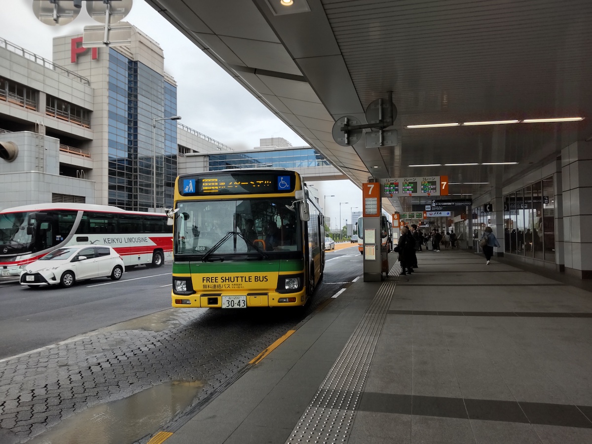 A yellow bus arriving at an airport bus stop to pick up waiting passengers