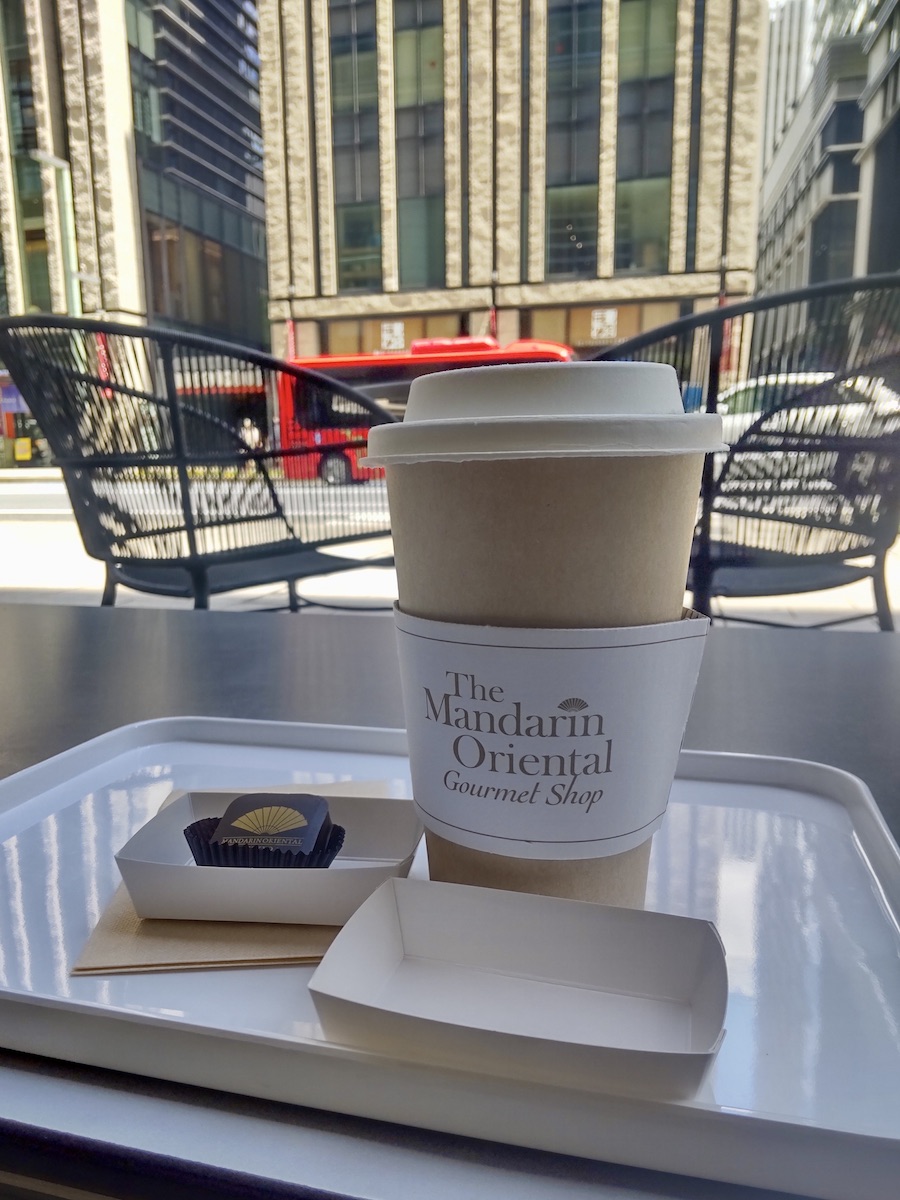 A paper cup with a lid and a single square chocolate with a road in the background