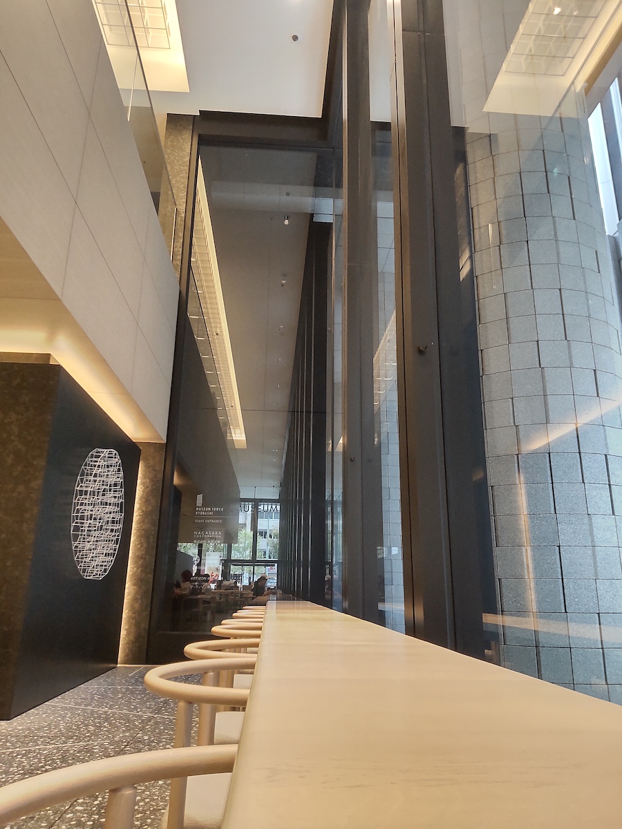 A glass-walled space featuring a high ceiling and a long table stretching into the distance