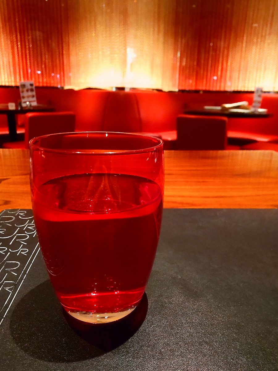 A glass of water in a red tumbler with a red interior in the background