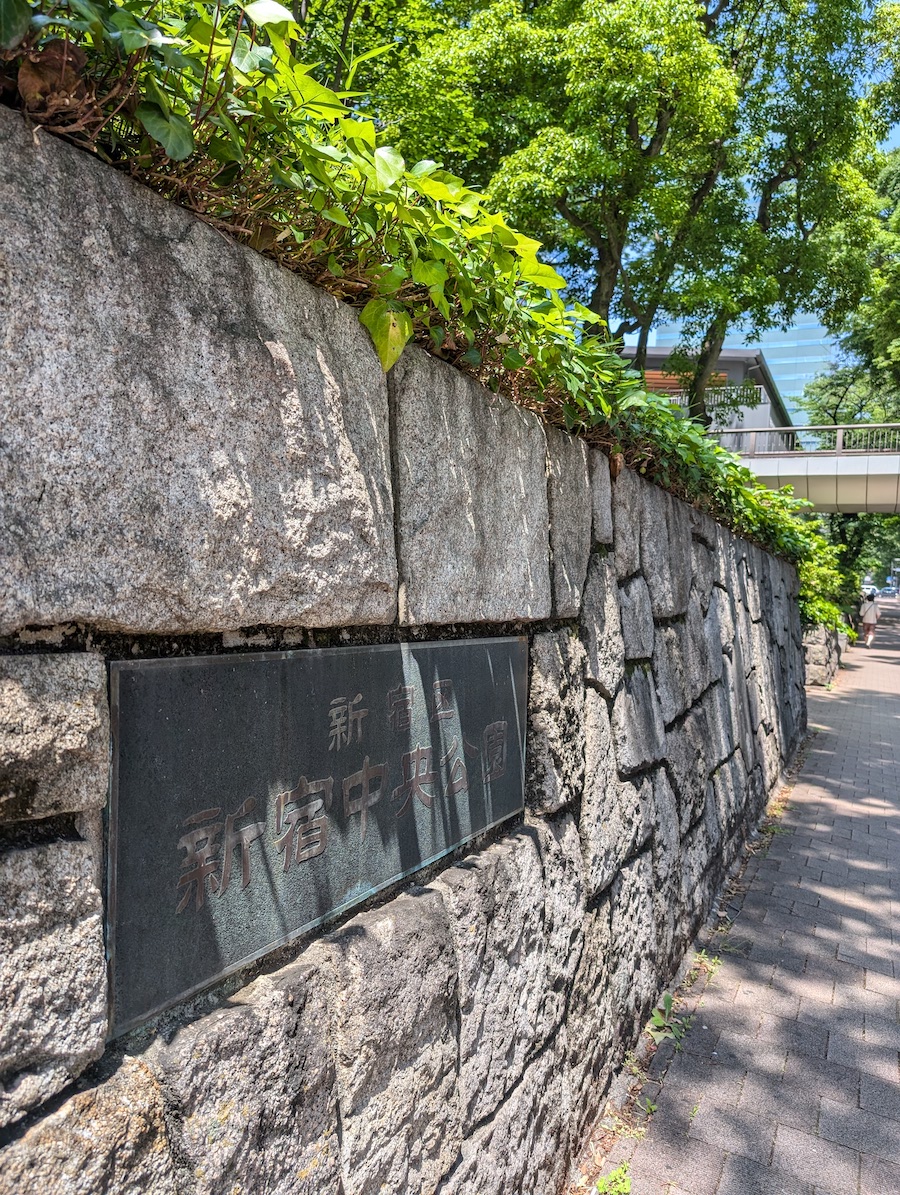 A stone park sign standing on the ground beneath shaded green trees