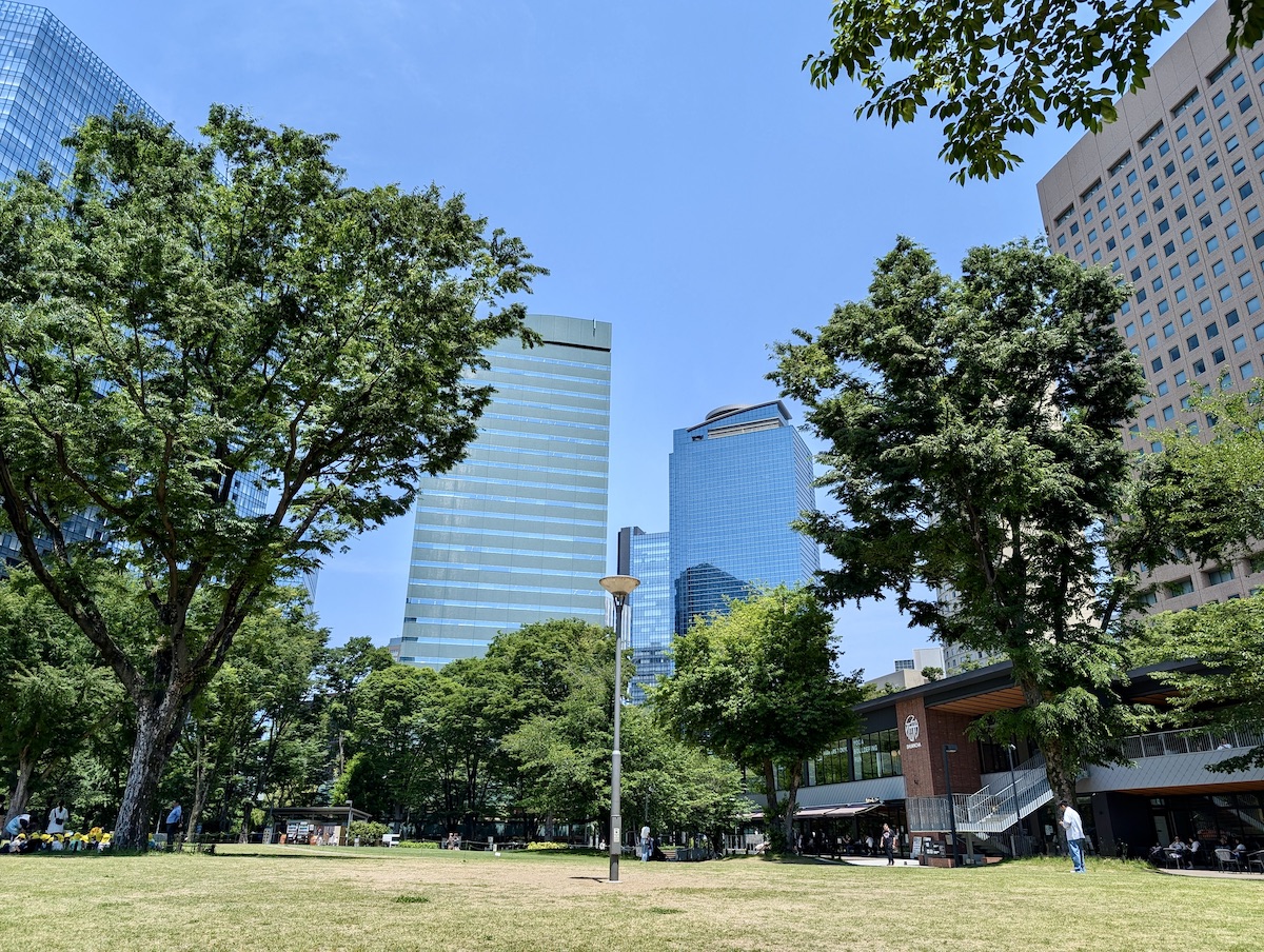 A two-story building in a park with tall city skyscrapers rising in the background