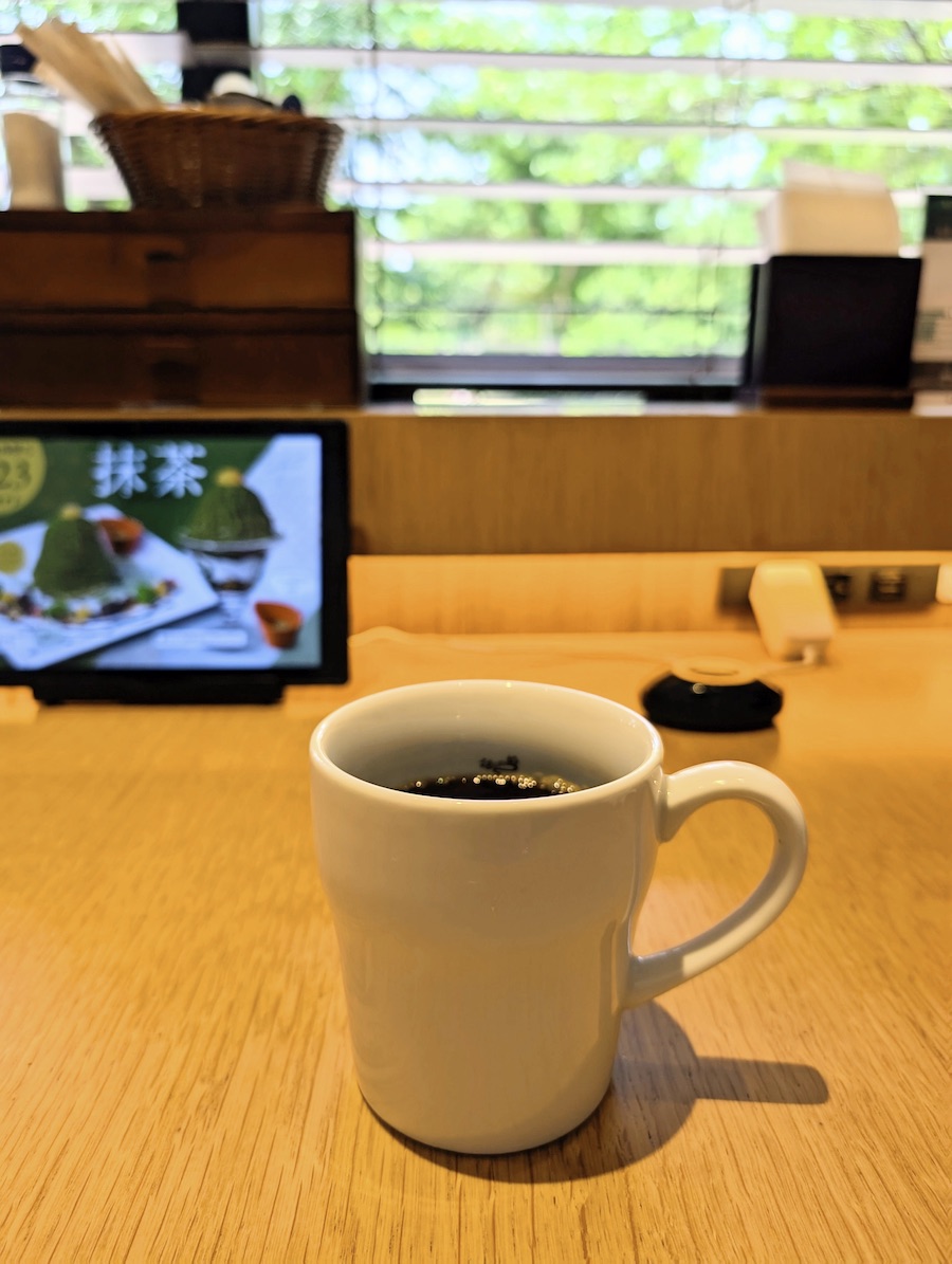 A coffee cup on a counter table with green foliage blurring in the background
