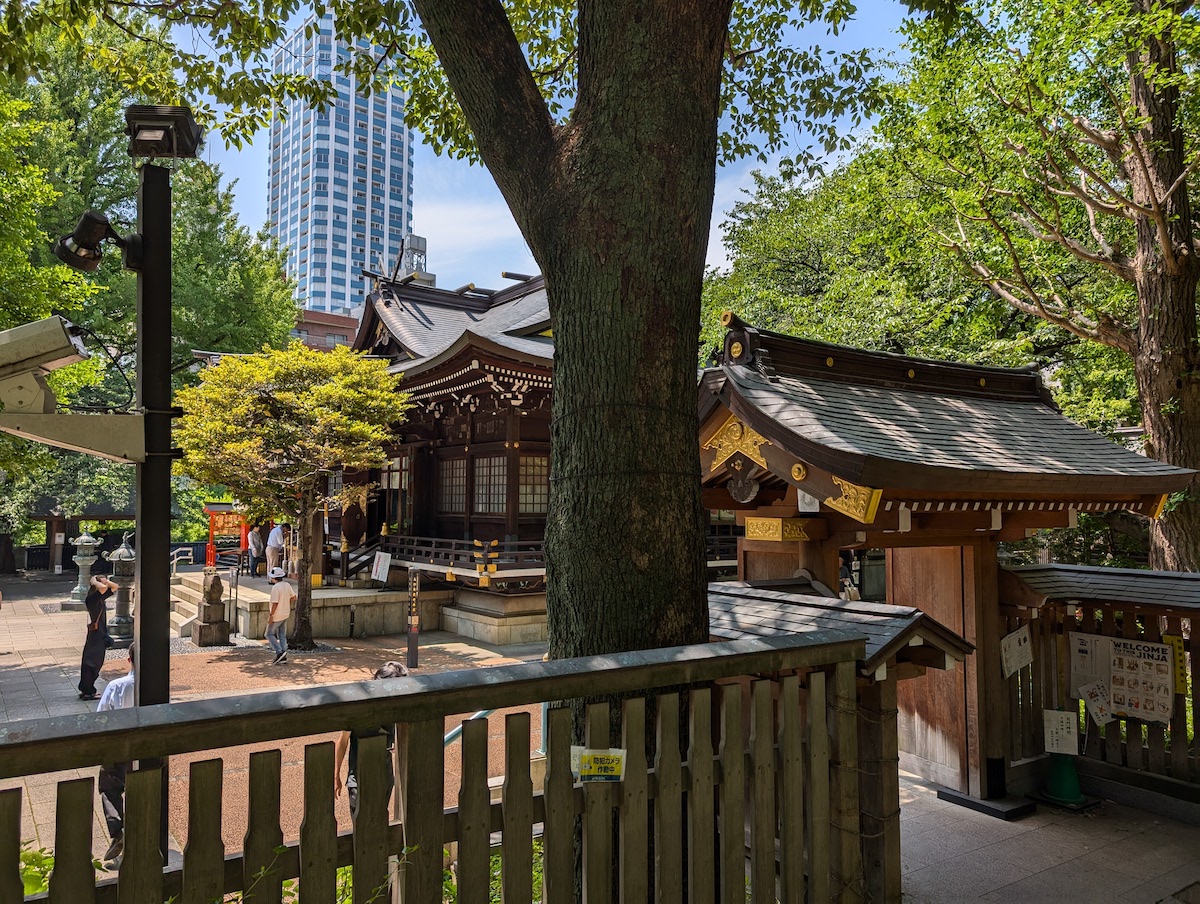A Japanese shrine standing quietly behind wooden fences and large green trees