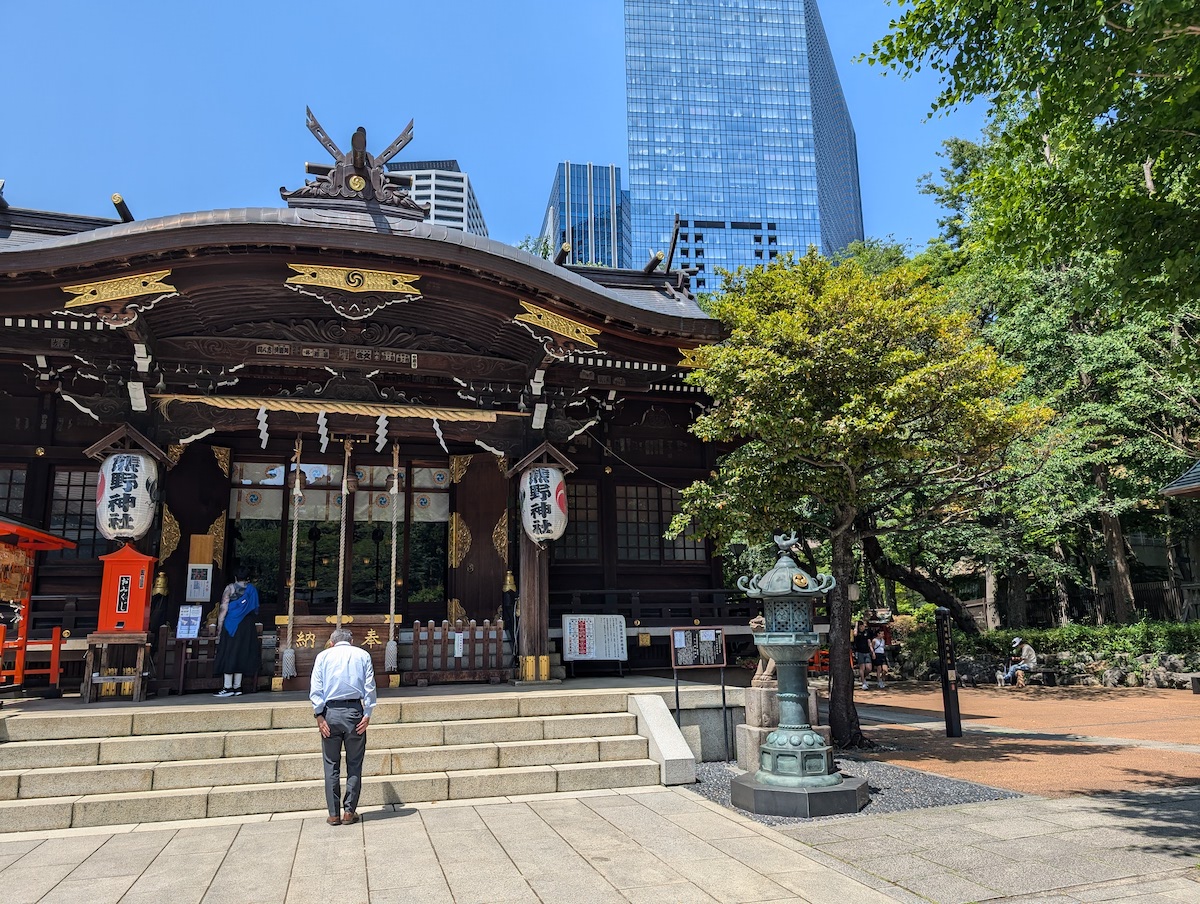 People praying at a traditional shrine with modern city skyscrapers rising in the background