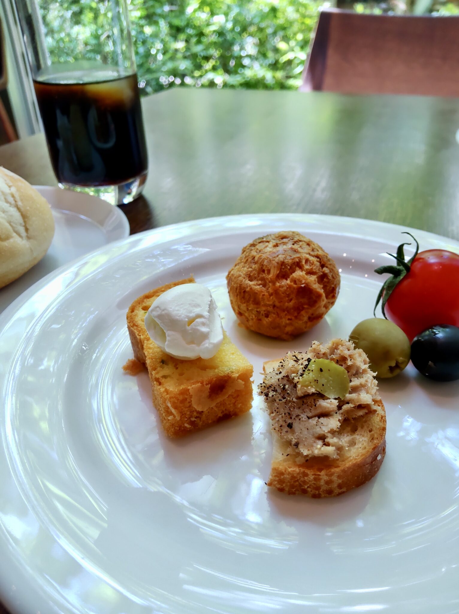 Assorted appetizers on a white plate with iced coffee behind