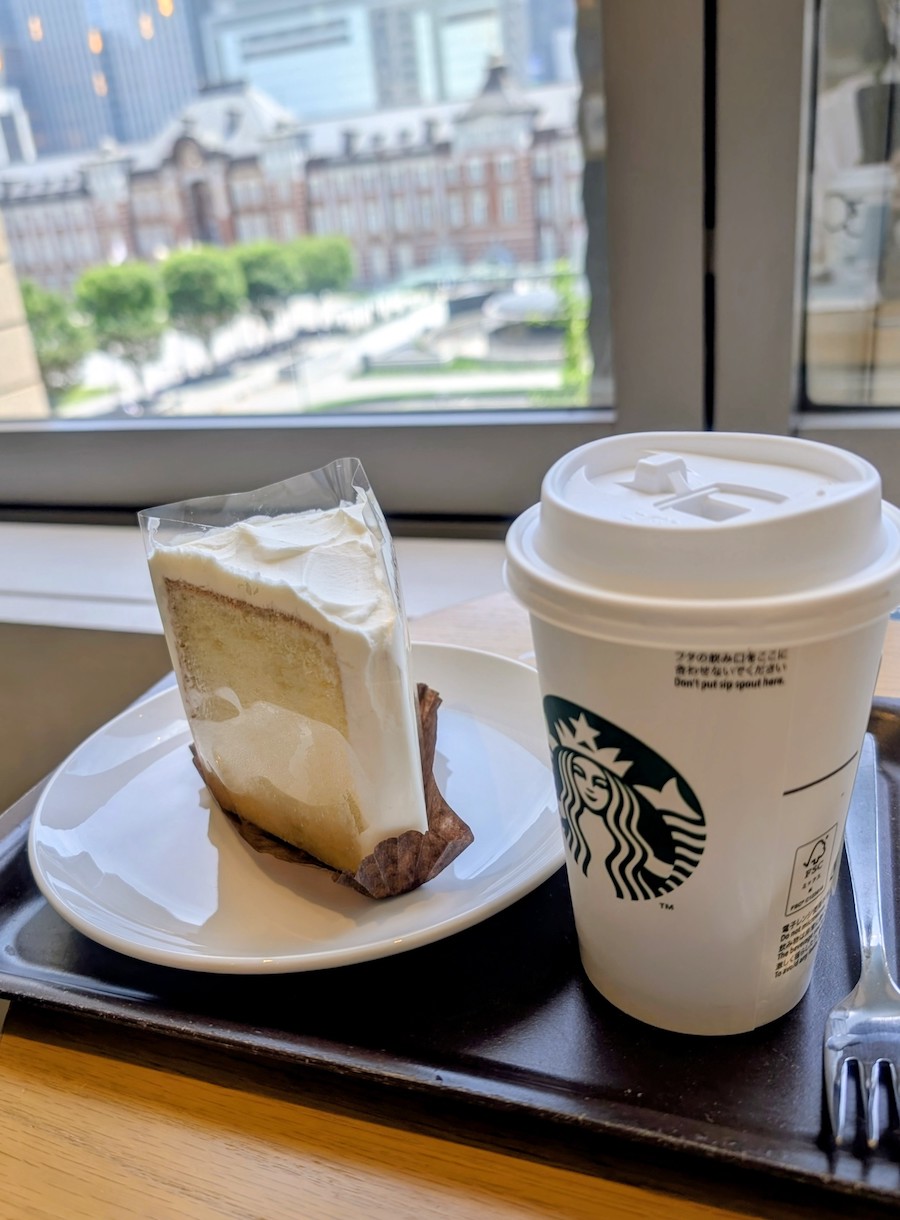 A Starbucks cake and drink with the brightly lit Tokyo Station visible beyond the window