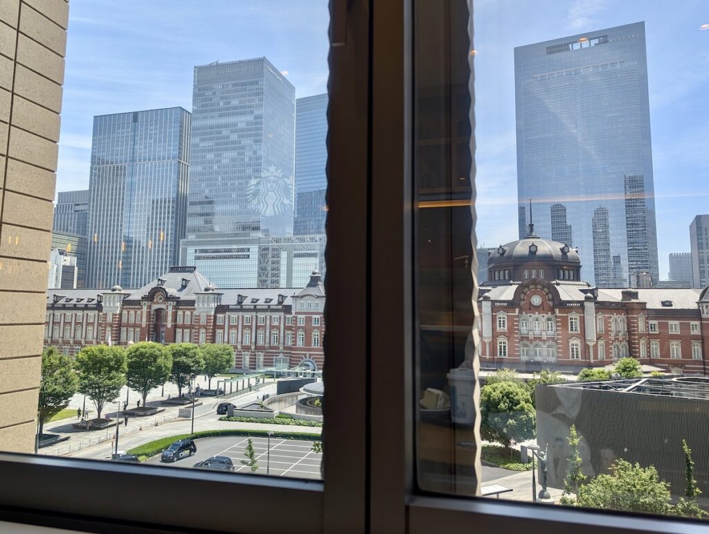 Tokyo Station, a bright plaza, and skyscrapers visible beyond a large glass window