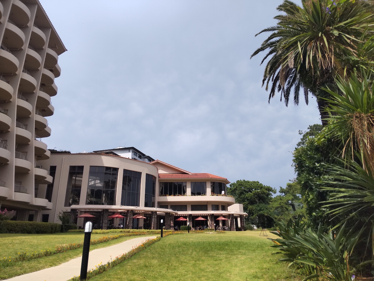 A resort hotel on the left, cafe tables behind, and many palm trees on the right