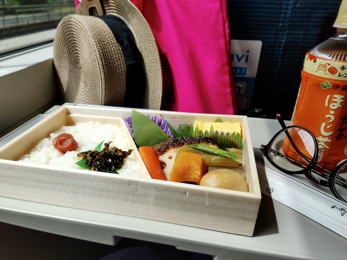 An open train bento box with rice on the left and Japanese side dishes on the right