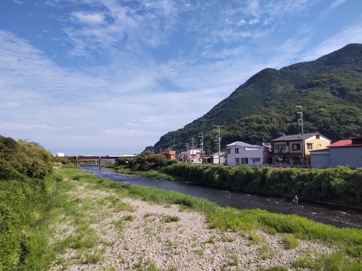 A green mountain under a blue sky, with a river and distant railway bridge