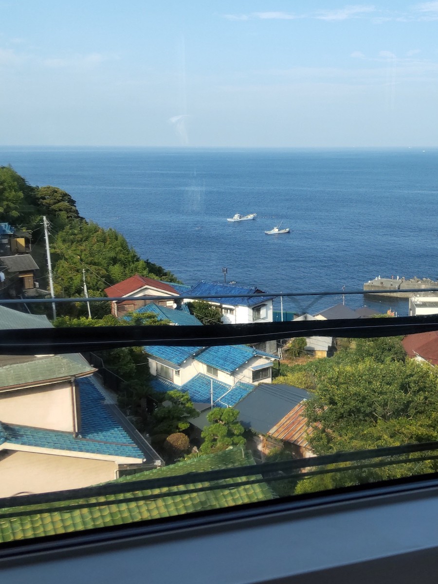 Two fishing boats on the sea with a traditional Japanese house in the foreground