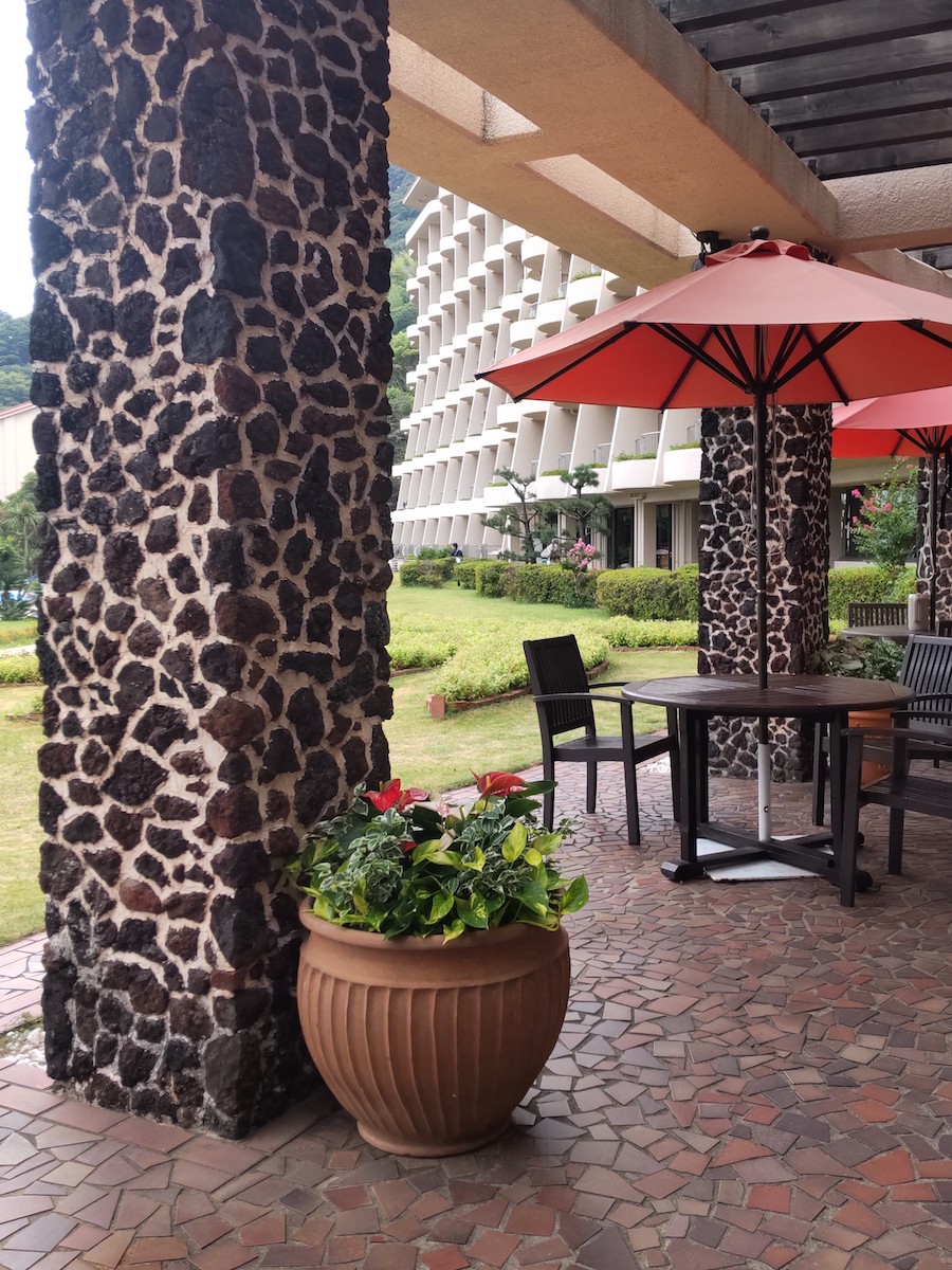 An outdoor walkway with vibrant flowers and cafe tables under red umbrellas