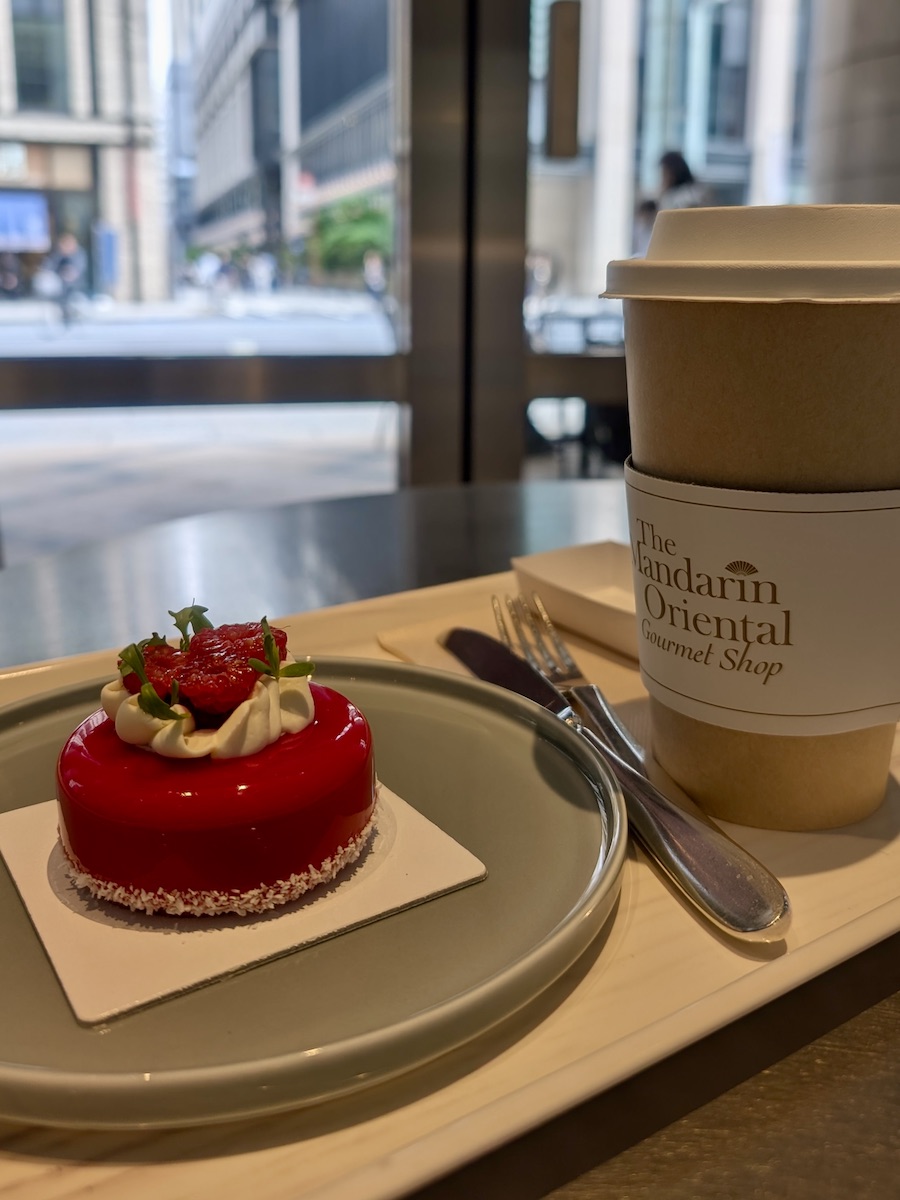 A beautifully made glossy red cake and a drink with a road visible beyond the glass window