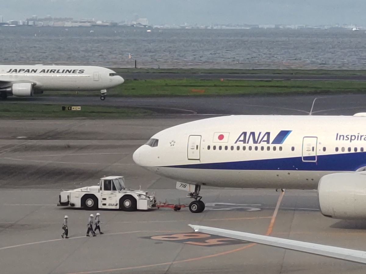 An ANA airplane attached to a towing tractor with staff walking on the tarmac
