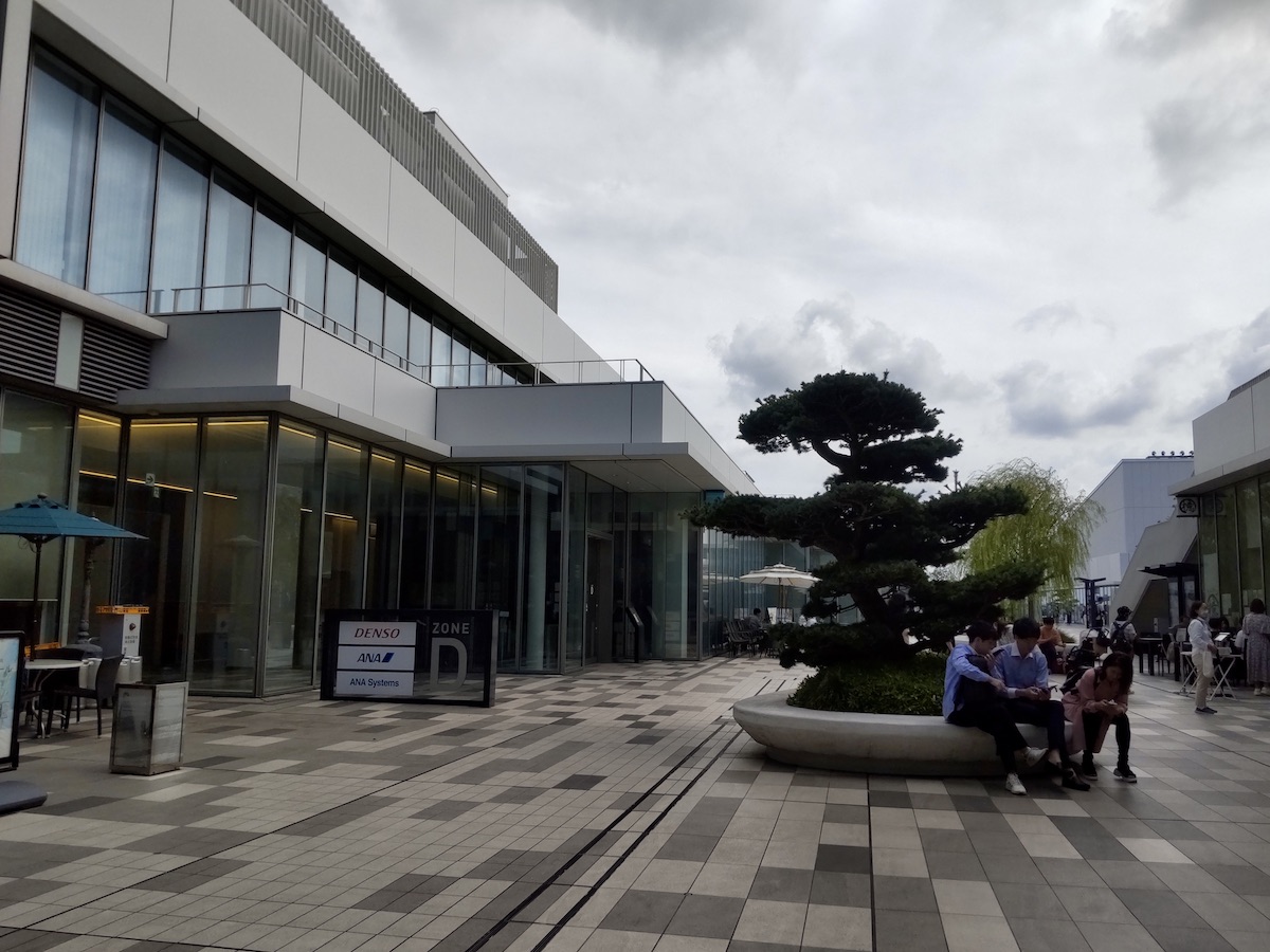A modern plaza with a pine tree and people resting on benches outside