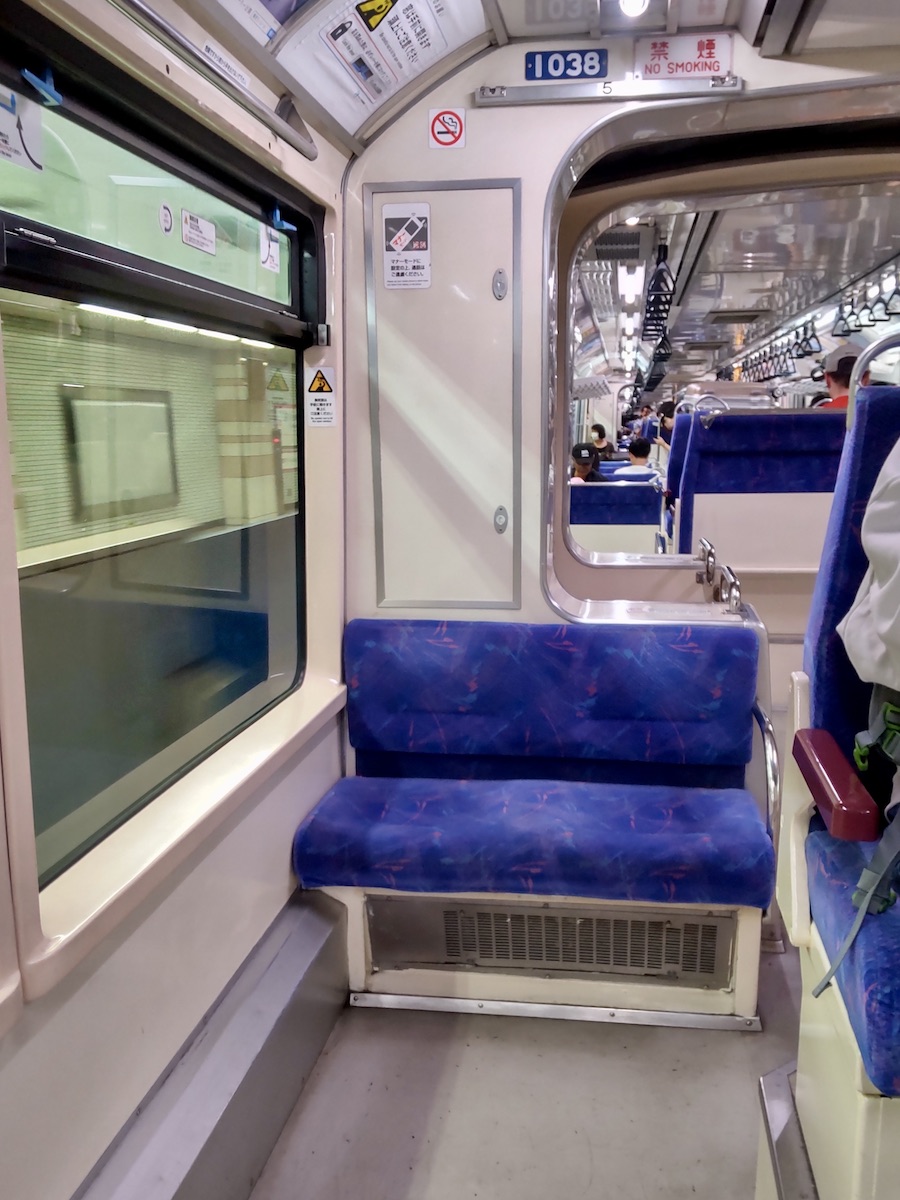 Inside a Japanese train showing blue seats and the interior corridor