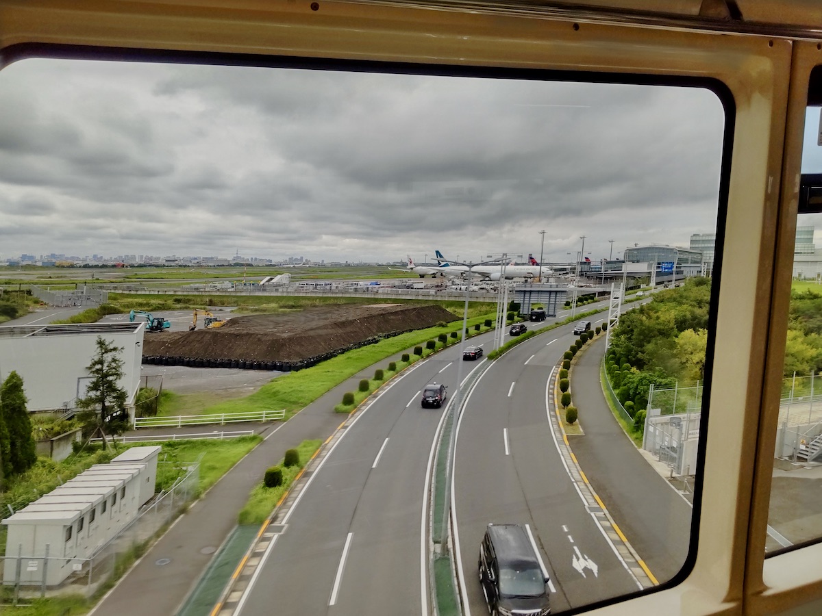 A view from a train window showing roads leading to Haneda Airport with parked airplanes