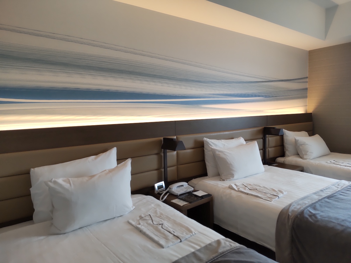 Clean comfortable beds in a hotel room with a blue ocean wave art wall