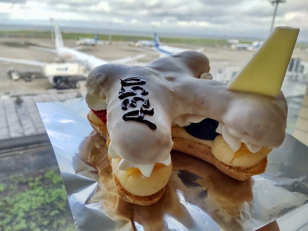 A cute airplane-themed dessert held in front of a window overlooking the airport