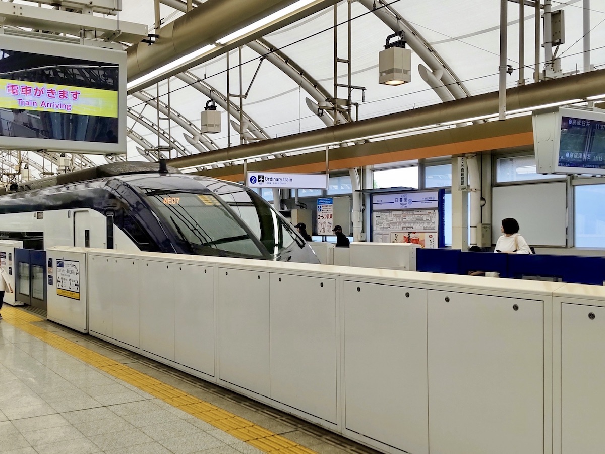 A modern white Japanese train arrives at a station with a high, covered canopy